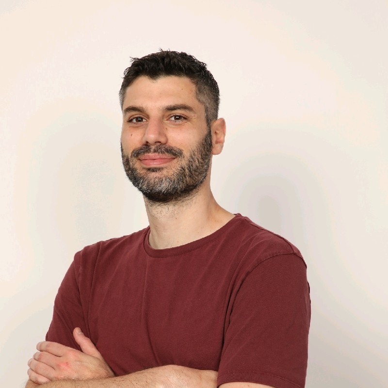 A man in a t-shirt with arms crossed looking slightly to the left.